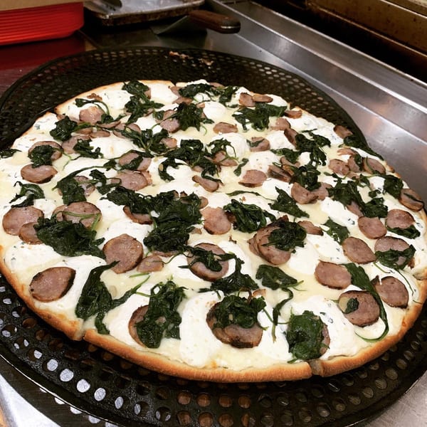 White pizza with ricotta cheese, spinach, and sausage on a black pizza pan.